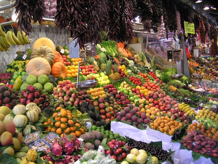 Fruit stall in Barcelona's Boqueria market with trays of cut fruit and juice cups under the market's iron structure